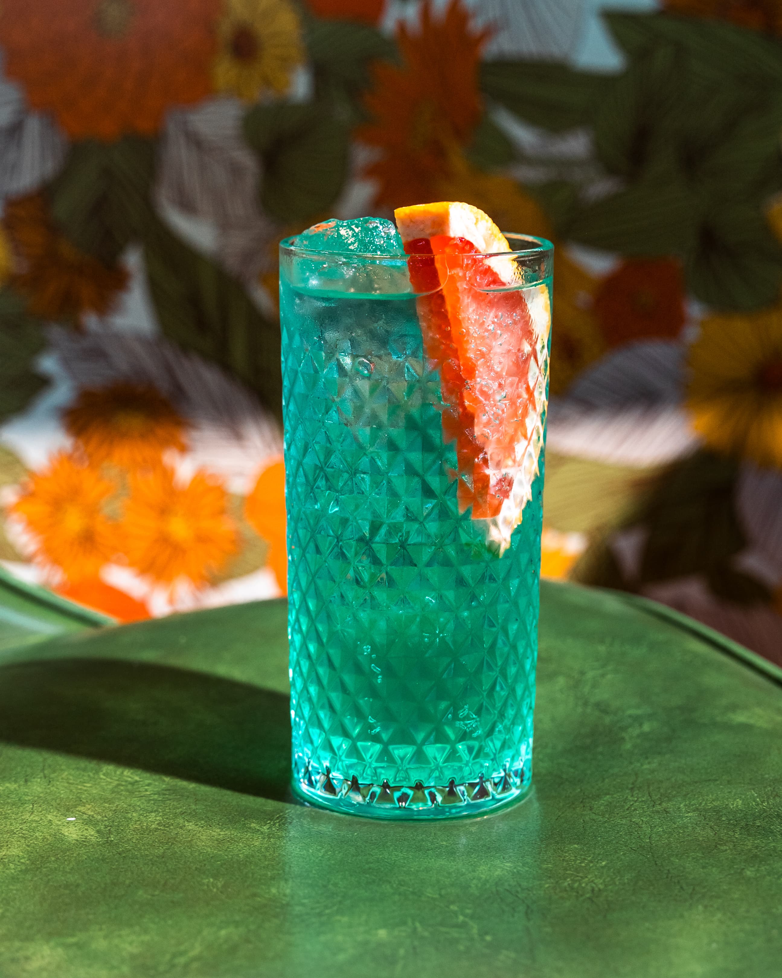 Turquoise cocktail in a textured glass with grapefruit garnish